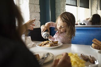 Mother with toddler daughter pouring ketchup in diner
