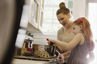 Mid adult mother giving daughter a helping hand in kitchen