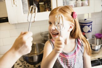 Girl and mother holding up whisks in kitchen