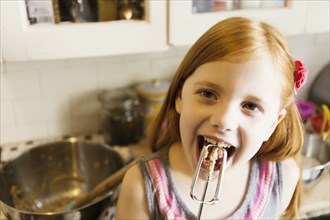 Girl licking mixture from whisk in kitchen