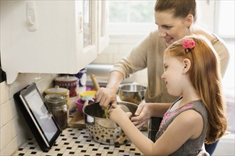Girl and mother looking at recipe on digital tablet in kitchen