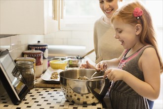 Girl and mid adult mother baking together in kitchen