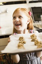 Girl holding up tray of biscuits in kitchen