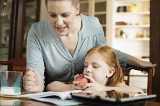 Mid adult mother helping daughter with homework at dining room table