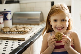 Portrait of girl eating biscuit in kitchen