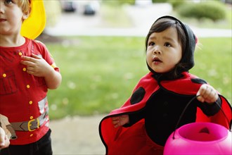 Girl and boy wearing fancy dress costumes with trick or treat bucket