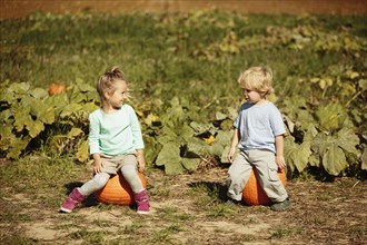 Brother and sister sitting on pumpkins in field