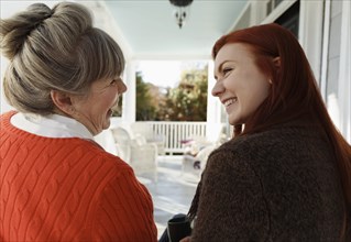 Senior woman and adult daughter laughing and chatting on porch