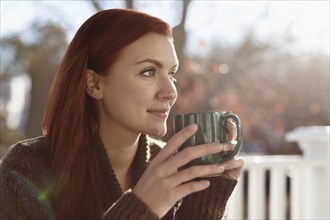 Young woman drinking coffee and gazing out from porch