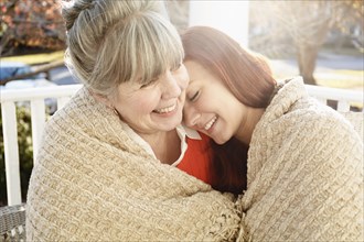 Senior woman and adult daughter wrapped in a blanket on porch