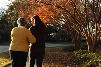 Rear view of senior woman and adult daughter strolling in suburban park