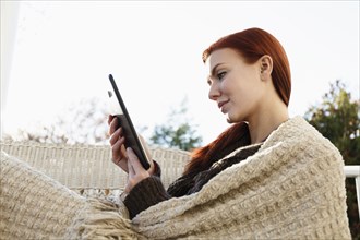 Young woman with red hair reading digital tablet on porch