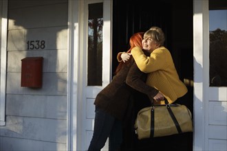 Senior woman and adult daughter hugging at front door