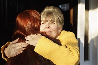Rear view of senior woman and adult daughter hugging at front door