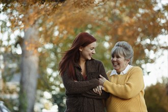 Senior woman and adult daughter strolling in suburban park