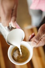 Coffee shop barista pouring milk into coffee