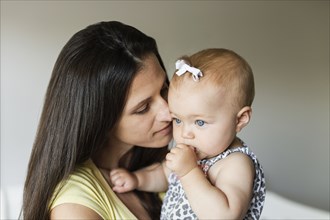 Portrait of mid adult mother with baby daughter sucking her thumb