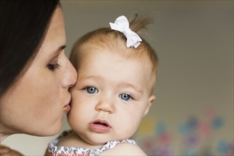 Close up of mid adult mother kissing baby daughter on cheek
