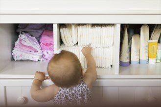 Rear view of baby girl reaching for diaper in cupboard