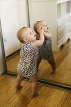 Baby girl leaning against mirrored wardrobe in bedroom