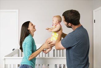 Mid adult couple holding up baby daughter in nursery