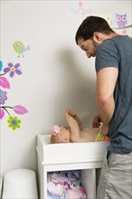 Mid adult man making faces whilst changing baby daughters nappy