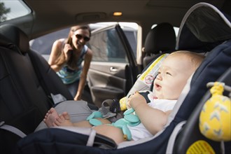 Mid adult woman checking safety belt on baby daughters car seat