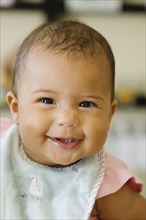 Portrait of baby girl wearing bib looking at camera smiling