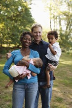 Family outdoors posing for photograph holding preschool boy and baby girl looking at camera smiling