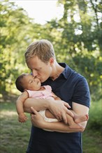 Father outdoors holding and kissing baby girl