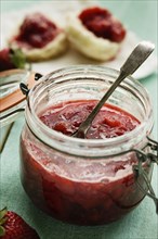 Jar of homemade strawberry preserve with teaspoon