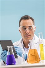 Scientist with digital tablet looking at liquids in beakers