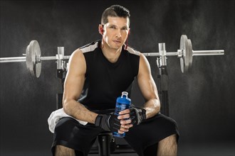 Muscular man training with barbell and holding water bottle