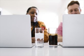 Water and soda in glasses between man and woman working on laptops