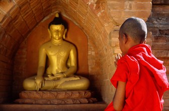 Novice monk praying in front of Buddha statue in temple