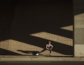 Woman stretching near brick wall in sunlight