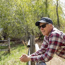 Senior farmer leaning on wooden fence near Sun Valley