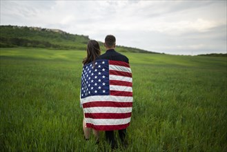 Rear view of young couple wrapped in American flag standing in wheat field