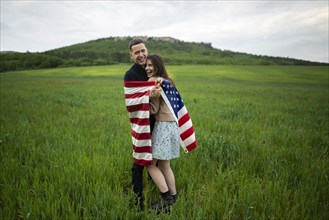 Smiling young couple wrapped in American flag in wheat field