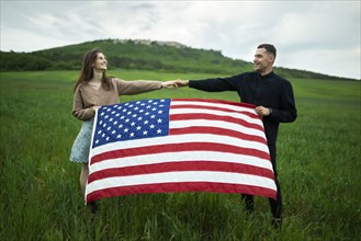 Young couple holding American flag in wheat field