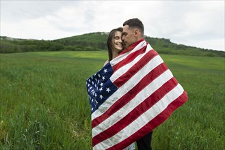 Young couple wrapped in American flag in wheat field