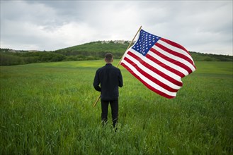 Rear view of man with American flag in wheat field