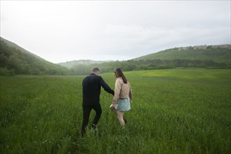 Rear view of young couple walking in wheat field in rain