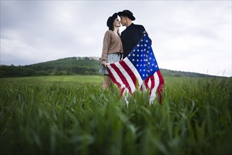 Young couple with American flag kissing in wheat field
