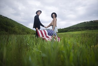 Young couple with American flag holding hands in wheat field
