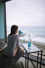 Rear view of woman drinking water in hotel with view on sea