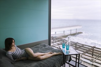 Woman reclining on bed in hotel with view on sea