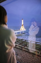Rear view of woman in bathrobe in hotel with view on sea at night