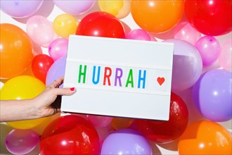 Woman holding sign saying Hurrah in front of balloon wall