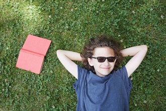 Boy lying in grass smiling with book